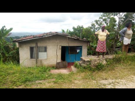 Angry residents of Allsides district, Trelawny, gather outside the home of 76-year-old Violet Walcott, retired farmer who was discovered chopped to death in her bed on Sunday night.