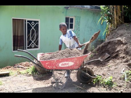 Nicolai Richards loads sand into a wheelbarrow at his home in Brandon Hill, Clarendon.