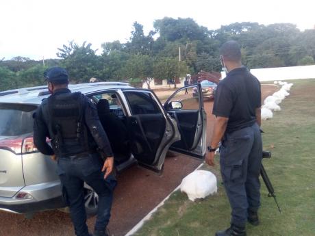 Police officers search a car at the Meadowrest Memorial Gardens in St Catherine yesterday after responding to reports of shots being fired during a clash involving mourners, workers and security personnel. 