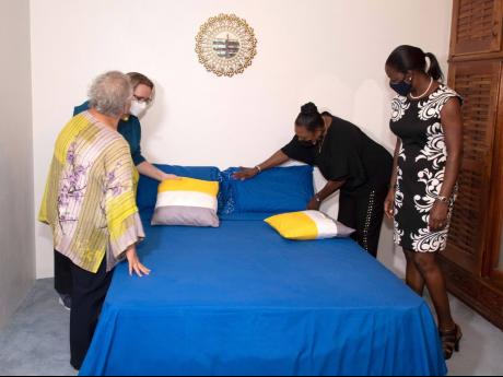 Minister of Culture, Gender, Entertainment and Sport,  Olivia Grange (second right), fluffs a pillow during a tour and opening of the second government-run shelter for women victims of domestic abuse. Sharing the moment are (from left) director of the UNFPA Caribbean Office, Alyson Drayton; the High Commissioner of Canada, Emina Tudakovic (partially hidden); and programme manager of the European Union Delegation to Jamaica, Vanna Lawrence.