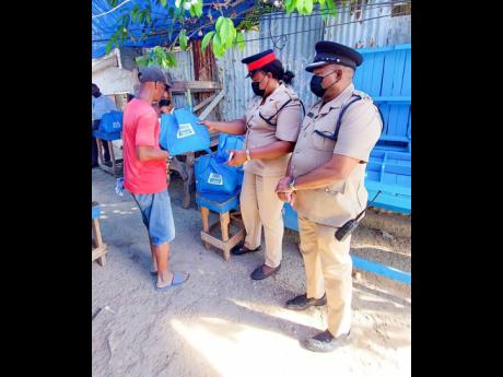Credit: Contributed Senior Superintendent Marlon Nesbeth (right) and Inspector Claudia Bailey-Finlayson hand out care packages to residents on Red Hills Road.