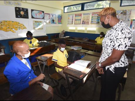 Education Minister Fayval Williams (left) and Juliet Cuthbert-Flynn (right) Member of Parlliament, St Andrew West Rural, look on as Omarie Leslie (centre), a student of Rock Hall Primary School leafs through a textbook on Tuesday. The officials visited the school to present a printer, which was donated by the Usain Bolt Foundation on Tuesday.