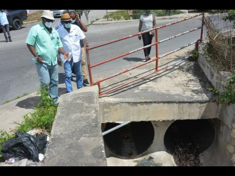Minister without Portfolio in the Ministry of Economic Growth and Job Creation Everald Warmington (second left) and Member of Parliament for St James Central Heroy Clarke (left) examine a drain in Green Pond, St James, during a tour on Tuesday.