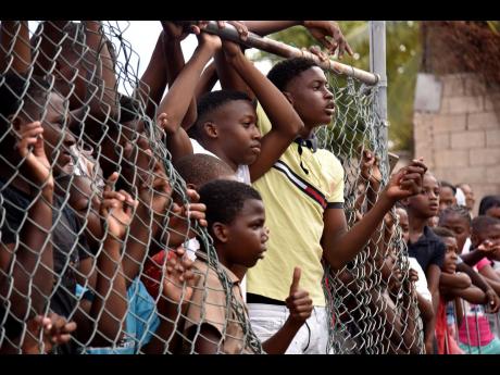 Credit: Kenyon Hemans These youngsters found the perfect spot — a hole in the fence — from which they watched as the Duke of Cambridge, William, put his football skills on display during a tour of Trench Town yesterday.