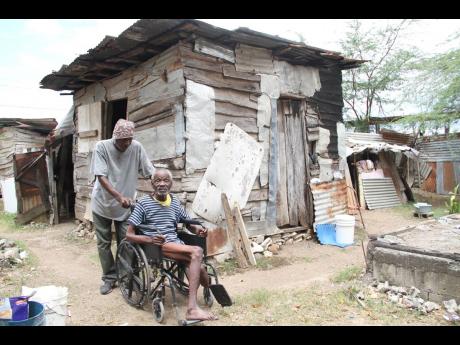 Albert Flash assists Harvey Brown to get around his yard, as they talk about the rundown house in which the disabled man has to live.