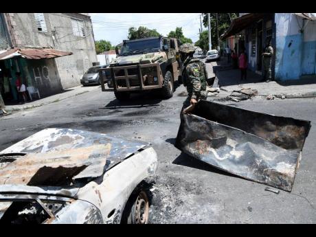 A member of the Jamaica Defence Force moves debris after residents of Denham Town blocked the roadway yesterday during another protest at the shooting death of Horaine Glenn by soldiers last Saturday.