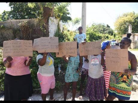 Residents of the Gutters community in St James hold up placards during a demonstration in the area on Tuesday, as they protest the recent death of 11-year-old Jason Bryan Jr who was hit by a car along the roadway on Sunday and died at hospital the following day.