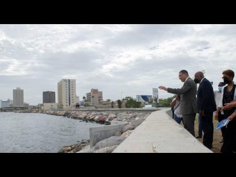 Prime Minister Andrew Holness (left) waves to a fisherman out at sea at the official handover ceremony for the Port Royal Revetment Project adjacent to the Breezy Castle Sports Complex on Wednesday in downtown Kingston. Looking on are Dr Wayne Henry, chairman of the Jamaica Social Investment Fund, and Imani Duncan-Price, who represented the Opposition Leader.