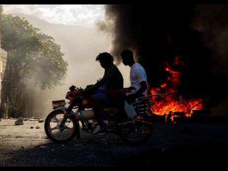 Men on motorcycle pass a burning barricade.