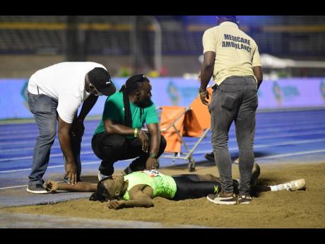 Long jump world champion Tajay Gayle lies in agony in the sandpit as medical officials tend to him after an injury during the JAAA National Senior Championships at the National Stadium in Kingston on Saturday night.