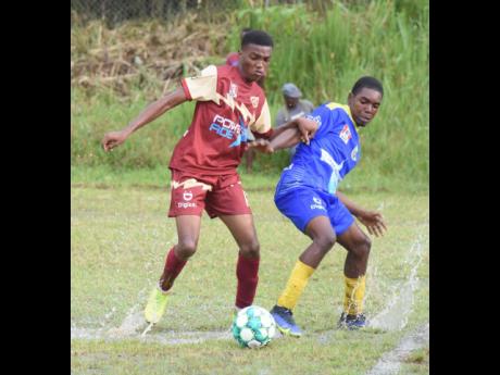 Herbert Morrison Technical’s Terrell Nelson (left) and Cedric Titus’ Christopher Walters battle in a puddle for the ball during their ISSA/daCosta Cup football match at Cedric Titus yesterday. Cedric Titus won 3-0.