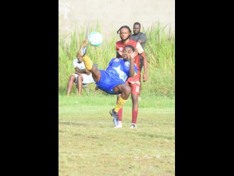 Cedric Titus’ Christopher Walters (left) tries an overhead shot at goal as Herbert Morrison Technical’s Jay-Dan Chambers watches  during their ISSA/Digicel daCosta Cup football match at Cedric Titus on Wednesday. Cedric Titus won the match 3-0.