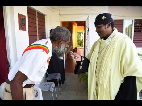 Haile Micka’el Cujo (left) bows and kisses the cross, which is being held by Abba Geereyesus Negat at the Ethiopian Orthodox Church Tewahado Church on Maxfield Avenue in Kingston yesterday.