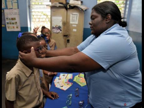 Credit: Ian Allen Tabrina Creary (right), comprehensive eyecare volunteer, checks glasses given to nine-year-old students.