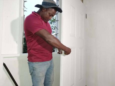 Credit: Tamara Bailey Principal of the Holmwood Technical High School, Hidran McKulsky, installing a door at the two-bedroom house built for a family of eight in Craighead, Manchester.