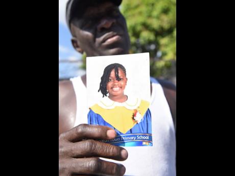 Anthony Hugh holds a picture of his dauhgter Liah Hugh, who died in a fire at her home on Giltress Street in Rollington Town, Kingston on Thursday.