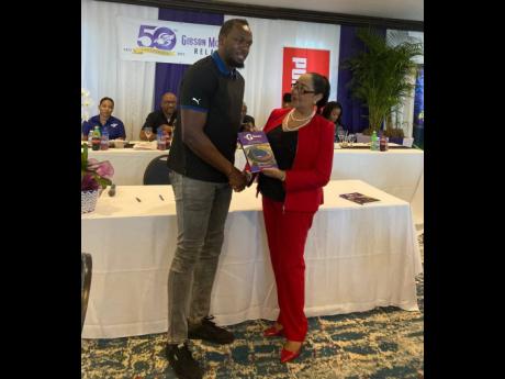 Credit: Sharla Williams Patron of the Gibson/McCook Relays Usain Bolt (left) receives a book depicting 40 years of the event’s history from Dr Marion Bullock Ducasse during a sponsors’ luncheon for its 50th anniversary at The Jamaica Pegasus hotel in New Kingston on Friday.