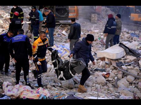 Credit: AP Two men carry a body from a destroyed building in Adana, southern Turkey yesterday.