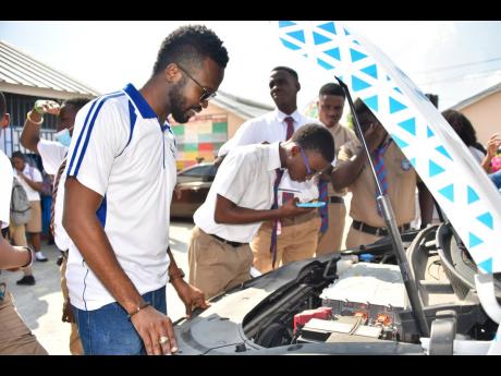 Credit: Contributed Head of the Department for Digital Transformation and Business Effectiveness at the Jamaica Public Service, Winston Blackwood (left), shows Holy Trinity High School student J’avar Dawes (second left) an electric car engine, while his peers look on.