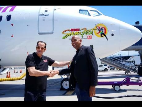 CEO of Caribbean Airlines, Garvin Medera (right), shakes hands with Reggae Sumfest promoter Joe Bogdanovich, on the revealing of the Reggae Sumfest decal, which stands out on the side of this Caribbean Airlines aircraft. 