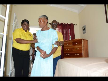 Minister of Local Government and Rural Development, Desmond McKenzie, and CEO of the Westmoreland Municipal Corporation, Marvalyn Pitter (left), assist Joyce Booth as she tours her new home.