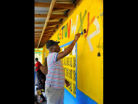 Assistant Commissioner of Police Calvin Allen, head of the Police Area 2, repaints the alphabet on the walls of the basic school.