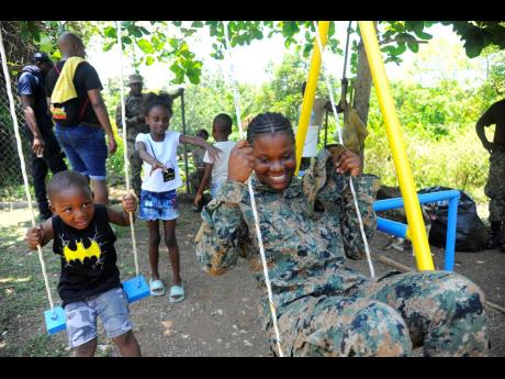 Young Jordain Green (left) looks on as Terika Graham (centre) pushes Private Blackstock after revamping the swings at the Parry Town Basic School during Labour Day.