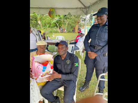 Constable Charlton Bailey (centre), of the Bamboo Police Station in St Ann, presents a gift package to centenarian Emilyn Rose of Forrest district, on the occasion of her 100th birthday. Woman Constable Shantay McLeggon looks on.
