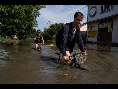 Residents try to ride their bikes along a flooded road after the Kakhovka dam blew overnight.