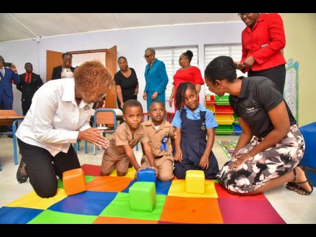 Executive Director of the Early Childhood Commission, Karlene DeGrasse Deslandes (left), and Senior Operations Manager of Digicel Foundation, Jodi-Ann McFarlane, play with children on the colour-coded mat inside the new inclusive classroom at Bethabara Infant School, Manchester, which was officially opened on July 5. 