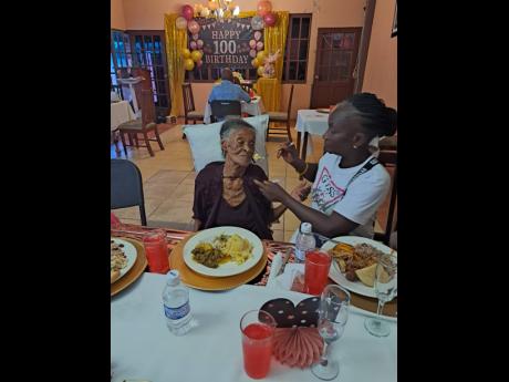 Credit: Rasbert Turner Eugenie Hall (right) feeds Myrtle Dowe at her celebration in Portmore, St Catherine on Saturday.