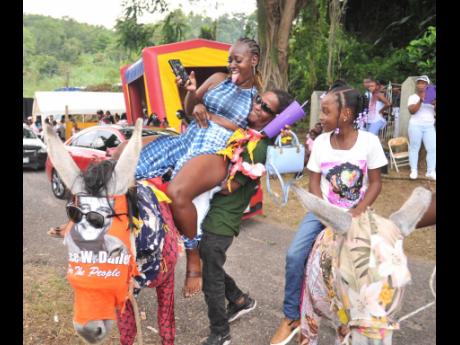 Shevaughn Gordon (left) is being assisted by Cleon McKenzie to mount WENDY, while young Carri McCalla sits comfortably in the saddle of her donkey.
