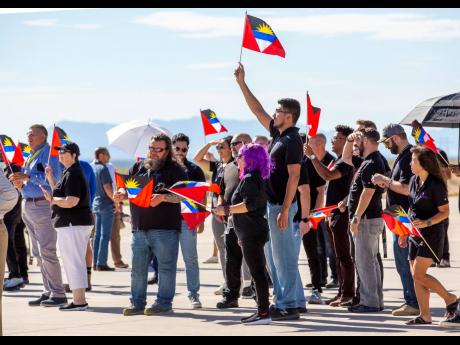Guests wave flags of Antigua and Barbuda while watching the return of Virgin Galactic's rocket-powered plane Unity at Spaceport America, near Truth or Consequences, N.M., Thursday, Aug. 10, 2023. Virgin Galactic is taking its first space tourists on a long-delayed rocket ship ride, including a British former Olympian and a mother-daughter duo from the Caribbean island. (AP Photo/Andrés Leighton)