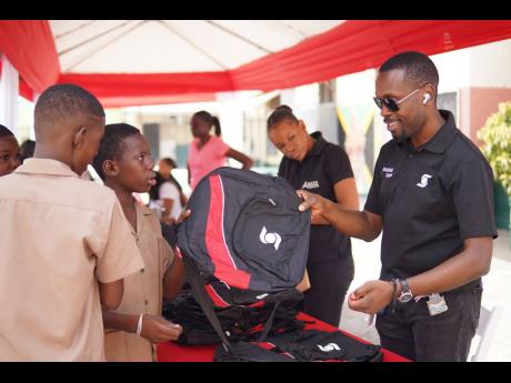 Christopher Samuels ( right), branch manager , Scotia Centre branch, passes out backpacks during a treat hosted by the Scotia Foundation at the Calabar Infant and Primary School last Friday.