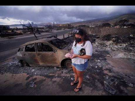Summer Gerling picks up her piggy bank found in the rubble of her home following the wildfire in Lahaina, Hawaii.  AP