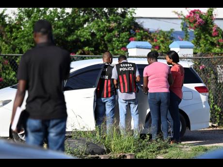Investigators on the scene of Monday’s double murder of a mother and daughter at the entrance of the National Solid Waste Management Authority on Spanish Town Road, St Andrew.