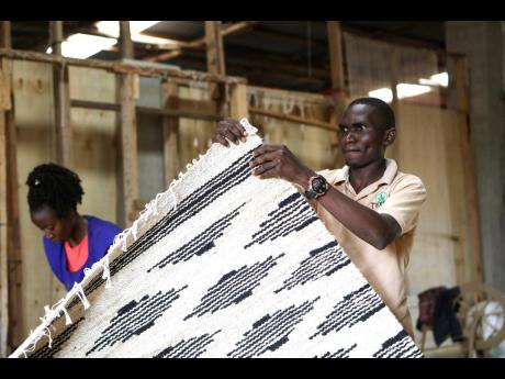 Manager of TEXFAD John Baptist Okello checks a handmade carpet woven from banana fiber threads at the factory in Sonde, Mukono district, Uganda. 