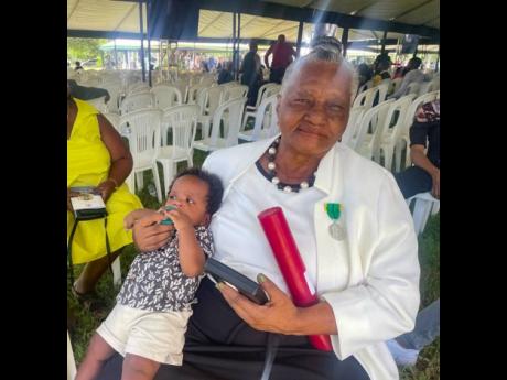 Mary Malcolm, a recipient of the badge of honour for long and faithful service, comforts her grandson after receiving her award at the Ceremony of Investiture and Presentation of National Awards Kings House in St Andrew.