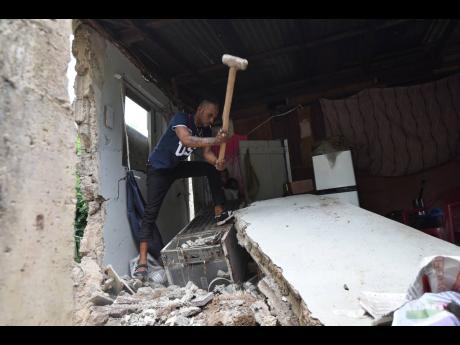 Credit: Ian Allen Joel Powell uses a sledgehammer to break a section of the house that collapsed during the earthquake.