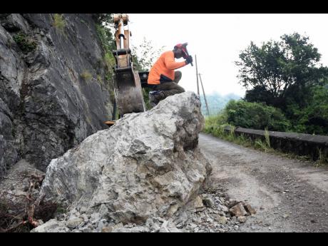 Renton Scott uses a hammer to try and chip away at a boulder that fell on the Woodford main road in rural St Andrew after Monday’s earthquake.