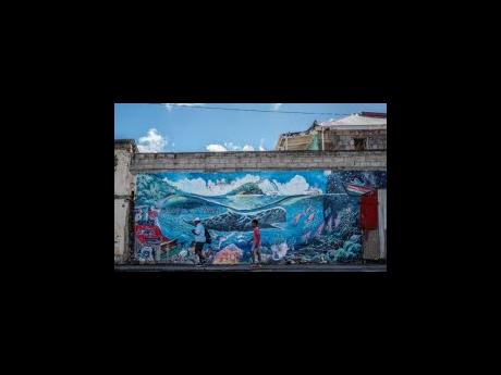 People walk past a mural of a whale created by artist Marcus Cuffi in Roseau, Dominica, on Sunday. (AP Photo/Clyde K Jno-Baptiste)