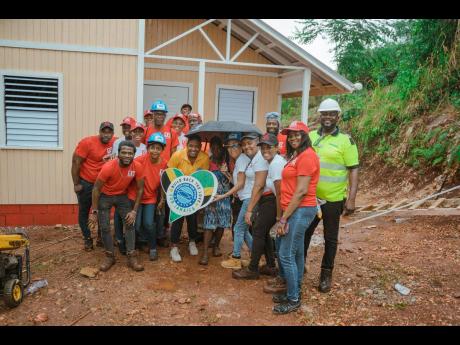 The Red Stripe and Food For The Poor Jamaica teams join Meghan Swaby for a photo-op at the entrance of her new house in Cross Keys, Manchester. 