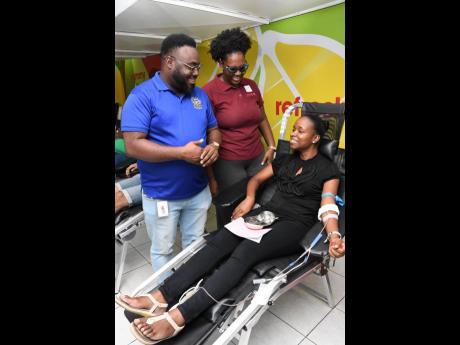 Jamar Howell (centre), chairman of the JN Sports and Social Club, and Toni Moy Stewart (centre), immediate past president of the Rotaract Club of Kingston (RCOK), speak with rotaractor, Shari Watson, as she prepares to donate blood at the 2022 staging of the RCOK’s Christmas Blood Drive, held at the JN Bank Chief Office in Half-Way Tree, St Andrew.