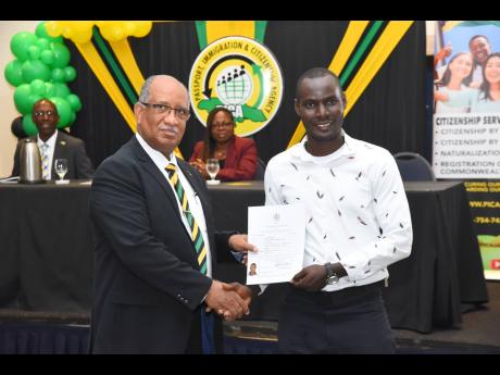 CEO of the Passport, Immigration and Citizenship Agency (PICA), Andrew Wynter (left), presents a Certificate of Citizenship to newly minted Jamaican, Richardson Louis, during PICA’s citizenship ceremony at The Jamaica Pegasus hotel in New Kingston, on Monday.
