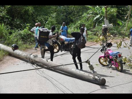 Motorcyclists who were trapped on one side of a downed utility pole in Golden Spring, St Andrew, last Friday assist each other to get their motor bikes over live power line. The pole fell when a truck got entangled with low-hanging wires along the Golden Spring to Mount Friendship roadway, leaving motorists stranded for nearly three hours.