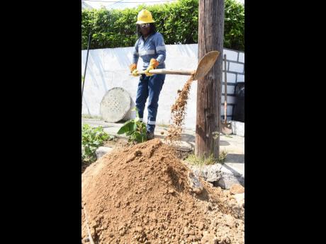 Blake, who loves the hands-on aspect of her job, digs a hole in preparation to replace a rotting pole in Independence City, Portmore, St Catherine.