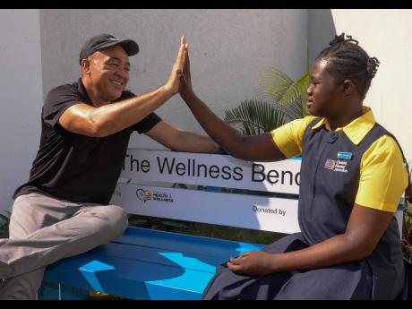 Minister of Health and Wellness, Dr Christopher Tufton, shares a high five with student at Christel House Jamaica, Chantoya Reggobie, while they sit on the new wellness bench installed at the school. Tufton visited the St Catherine-based institution on Wednesday for a wellness check-in, as part of the ministry’s #DoYourShare mental wellness campaign.