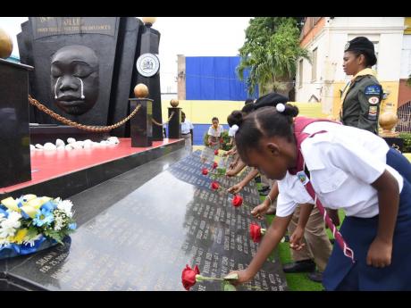 Jamaica Pathfinder Club member, Ceandra Howell, joins children in paying floral tributes to the youths who lost their lives under tragic and violent circumstances, during the Kingston and St Andrew Municipal Corporation’s Child Month ceremony at the Secret Gardens monument, downtown Kingston, on Sunday.
