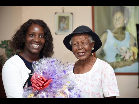 Maureen Byfield-Jarvis (left), parish organiser at the National Council for Senior Citizens in Kingston, presents Enid Bernard with a gift basket at her Harbour View home in St Andrew, in recognition of Centenarians Day, which was observed yesterday.