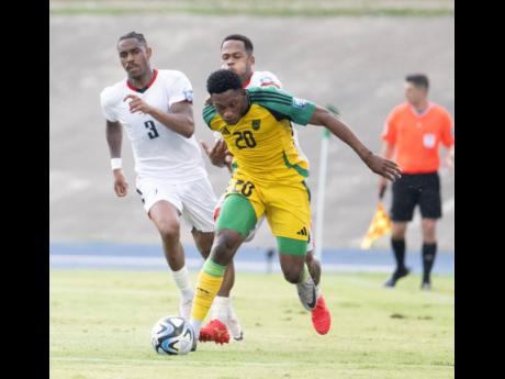 Jamaica’s Renaldo Cephas shields the ball from  Dominican Republic’s Ronaldo Vasquez while his teammate Junior Firpo (left) looks on. The action is from yesterday’s 2026 World Cup qualifying match at the National Stadium. Jamaica won 1-0.